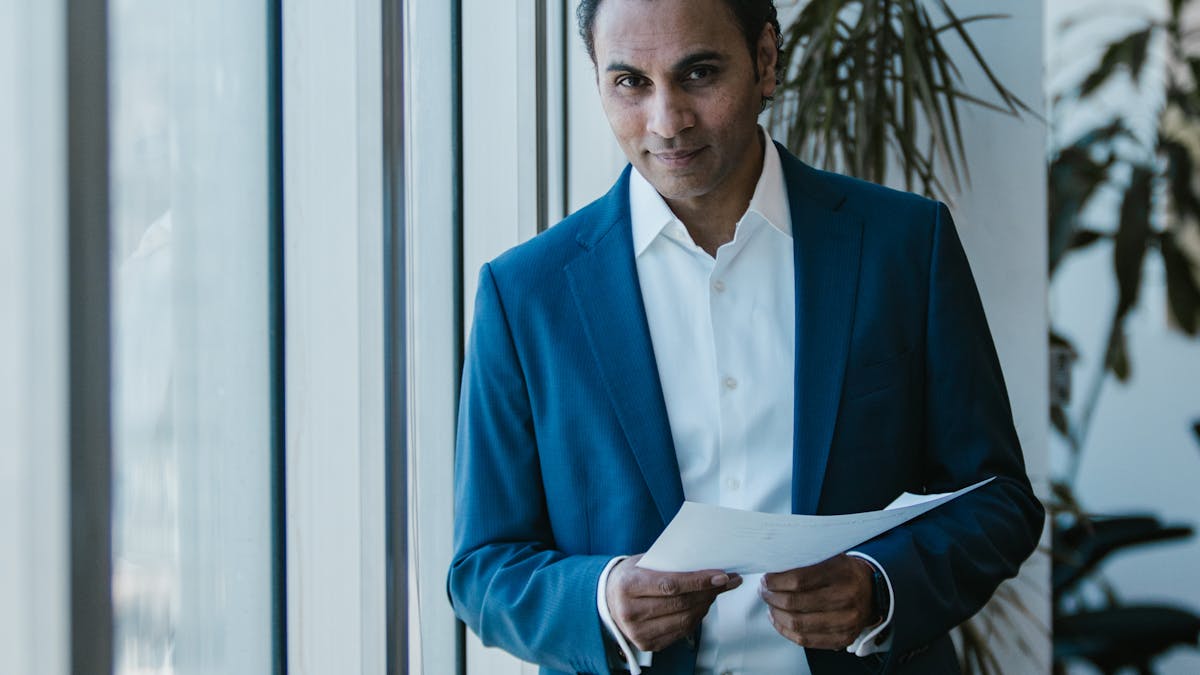 Indian businessman in blue suit holding a document by the office window