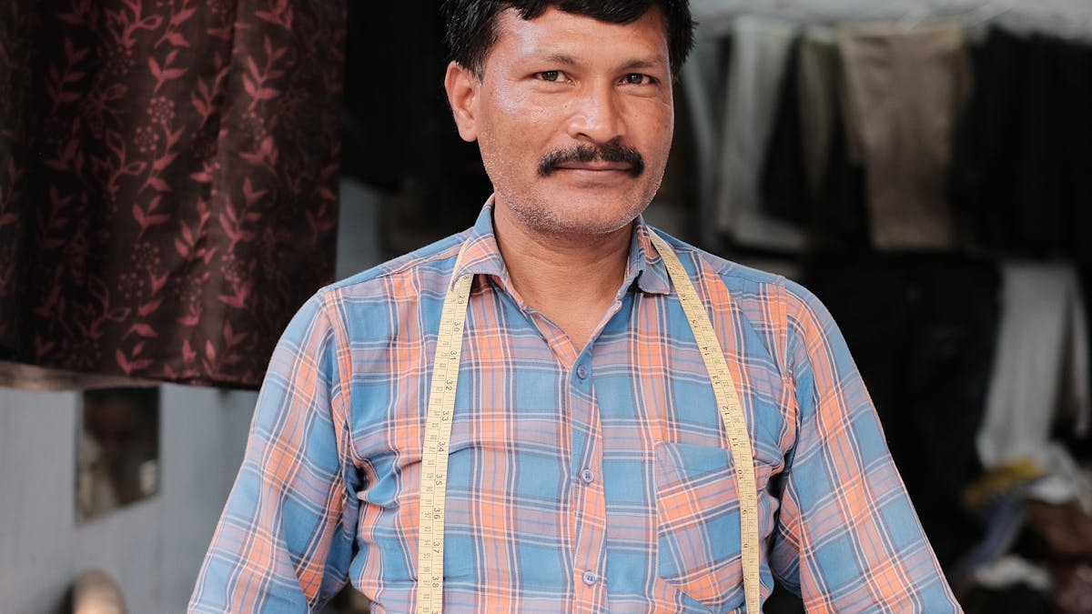 Indian tailor with measuring tape standing in front of his tailoring shop