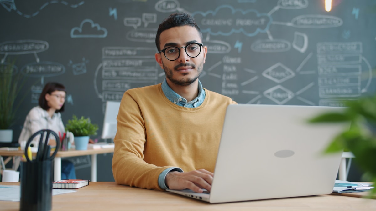 Indian man with glasses working on laptop in a modern coworking space