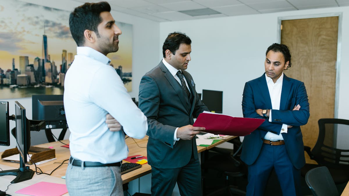 Three Indian businessmen in suits reviewing documents in a modern office &mdash; LLP partners