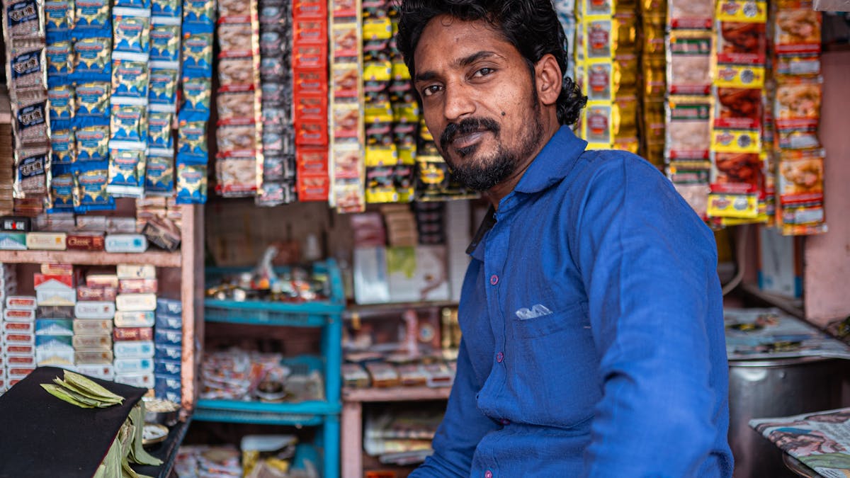 Indian shopkeeper at his pan and tobacco store with hanging product packets